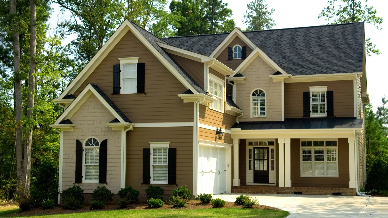 Brown two-story house with dark shingle roof and white garage door