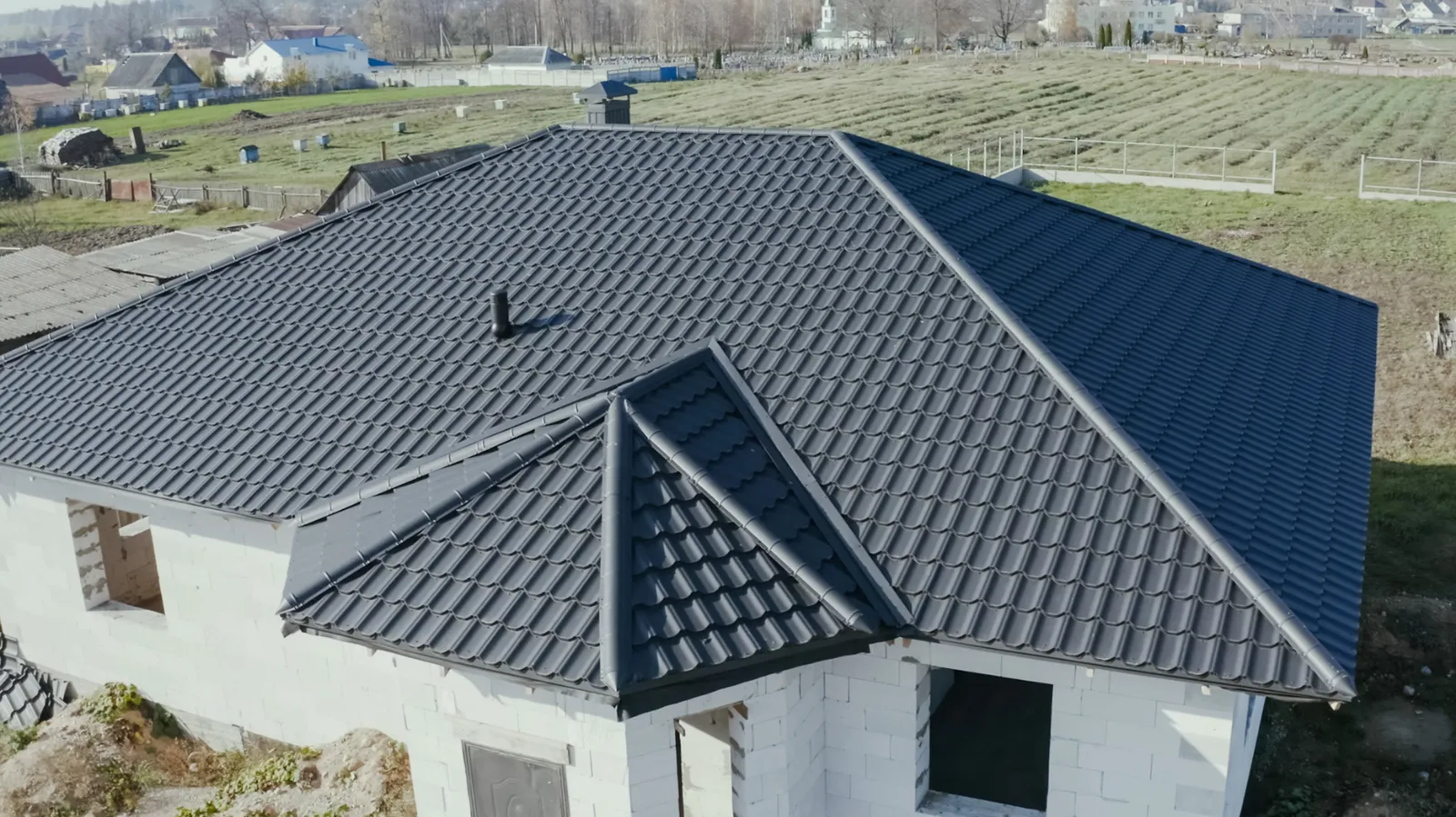 Block house with a dark metal tile hip roof and fields beyond